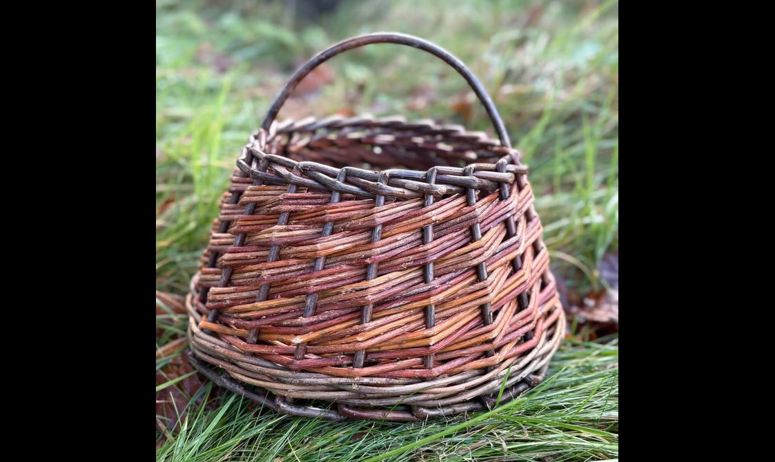 A small dark brown basket made of willow on the grass.