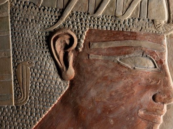 A Egyptian sculpture made of brown stone, showing a pharaoh's head with a prominent headdress and serpent motif.