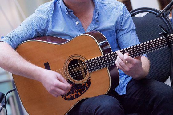 Close up of a musician in a blue shirt playing a guitar.