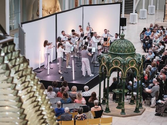 An orchestra is performing in the grand gallery at the National Museum of Scotland.