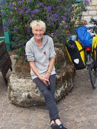 Image of a woman sitting on a rock, with purple flowers behind her.