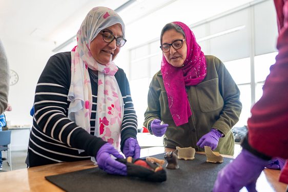 Two people wearing headscarves handling museum objects from the Ancient Egyptian collection