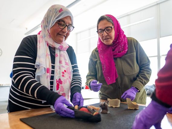 Two people wearing headscarves handling museum objects from the Ancient Egyptian collection