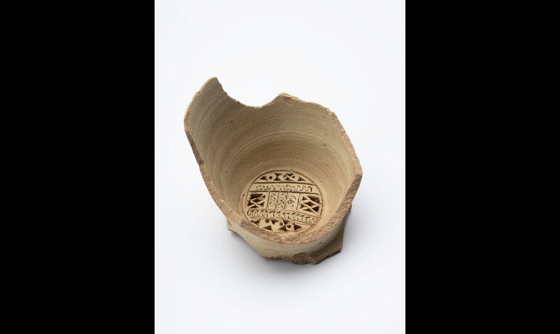 A portion of a terracota water vessel with an intricate carved design on the base.