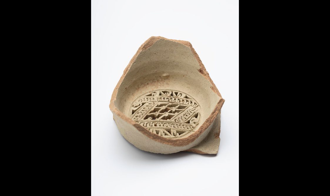 A portion of a terracota water vessel with an intricate carved design on the base.