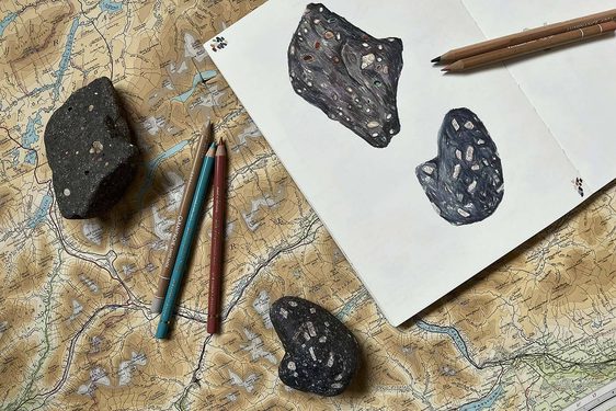Two fossils lying on a large map next to some coloured pencils and a sketchbook. The sketchbook contains illustrations of the fossils.