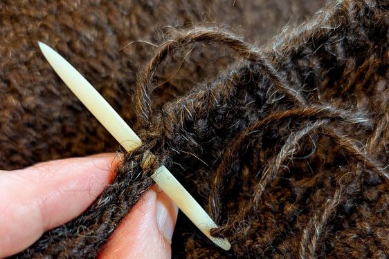 A hand holding a needle that has been threaded through brown wool fabric