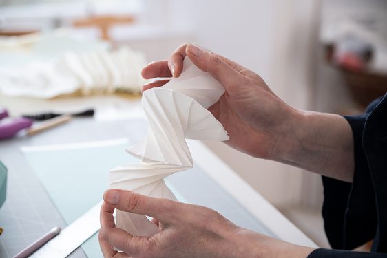 A pair of hands holding a paper folded intricately, almost like an accordion.