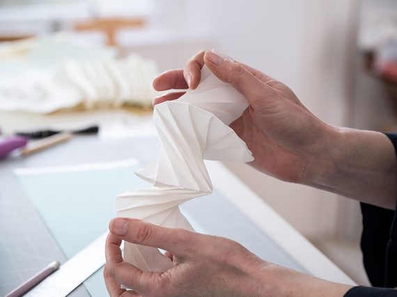 A pair of hands holding a paper folded intricately, almost like an accordion.