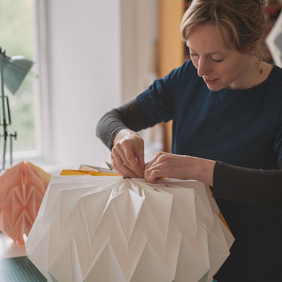 A woman folding a paper structure into a round shape in an airy studio.