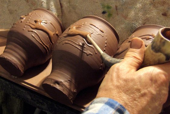 A potter adding finishing touches to a decorated clay pot
