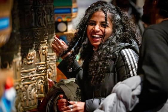 A person standing smiling next to a set of prayer wheels.