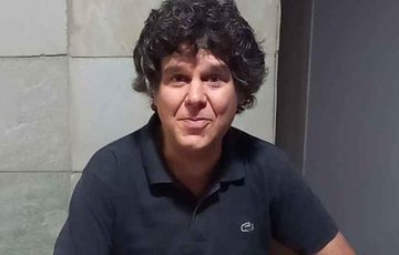A man in a dark polo shirt in front of a tile wall.