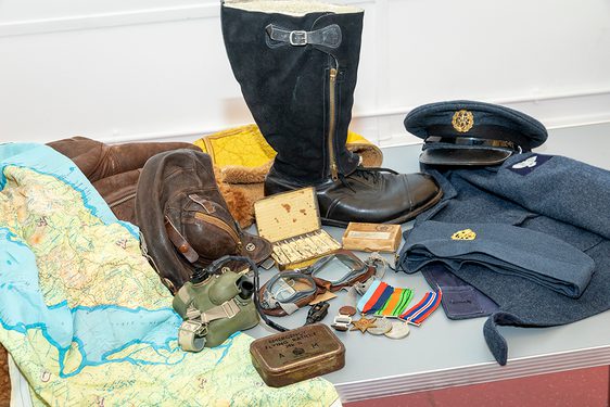 A group of objects from laid out together from the Second World War, including a map, brown satchel, war medals, and a navy blue pilot's clothing.