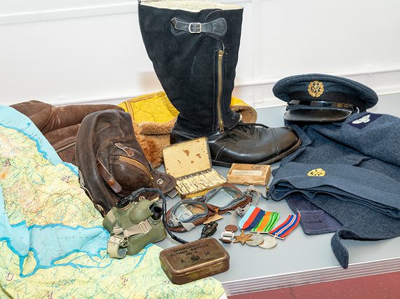 A group of objects from laid out together from the Second World War, including a map, brown satchel, war medals, and a navy blue pilot's clothing.