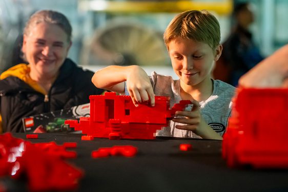 A parent and child play with red Lego bricks on a table.