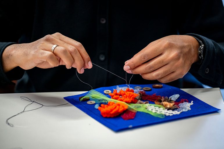 Close up of a pair of hands sewing together a colourful quilt square at a Sewing Hope workshop.