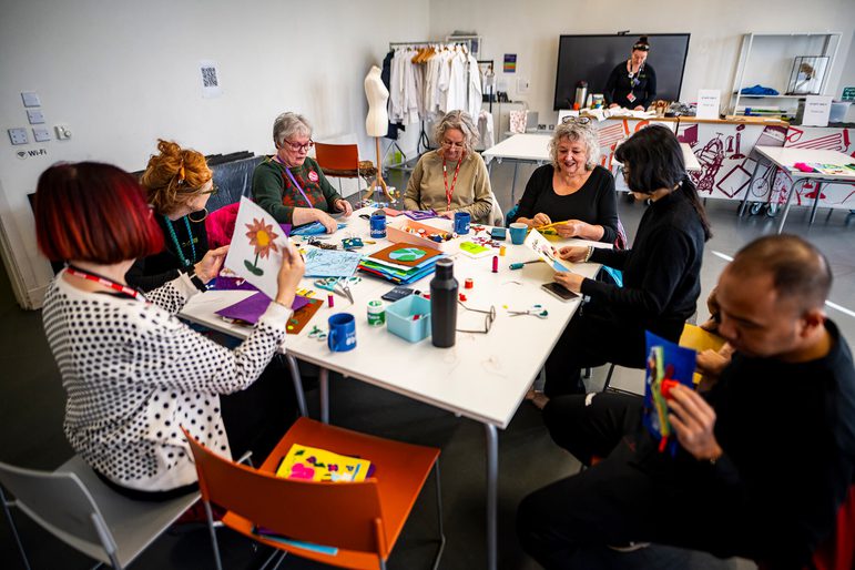 A group of adults from the Edinburgh Remakery sitting at a table sewing together colourful quilt squares.