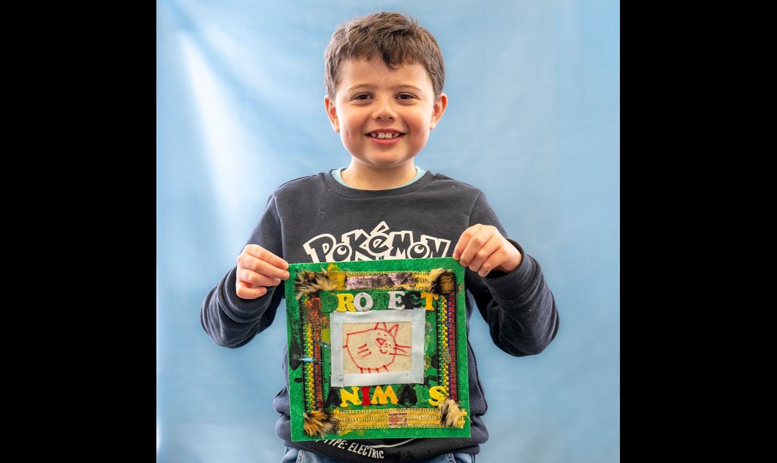 A young person is smiling directly at the camera, holding up a fabric quilt scare that say protect the animals.