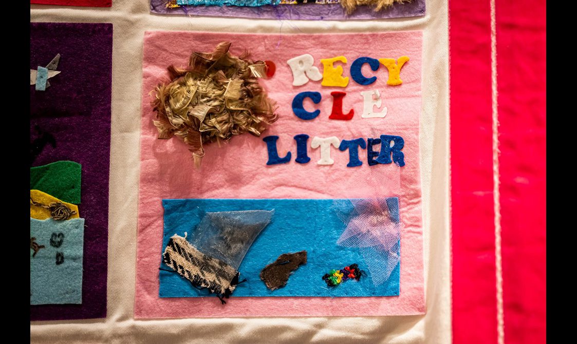 A pink quilt square with the message "recycle litter" spelt out in felt letters. Bits of fabric show pieces if litter in the ocean.
