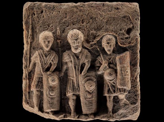 A sandstone sculpture with three legionaries holding shields and weapons