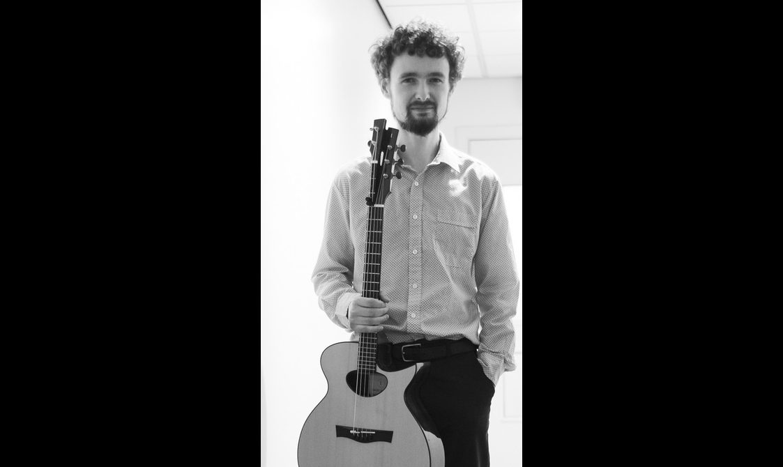 A man with curler hair stands holding a guitar.