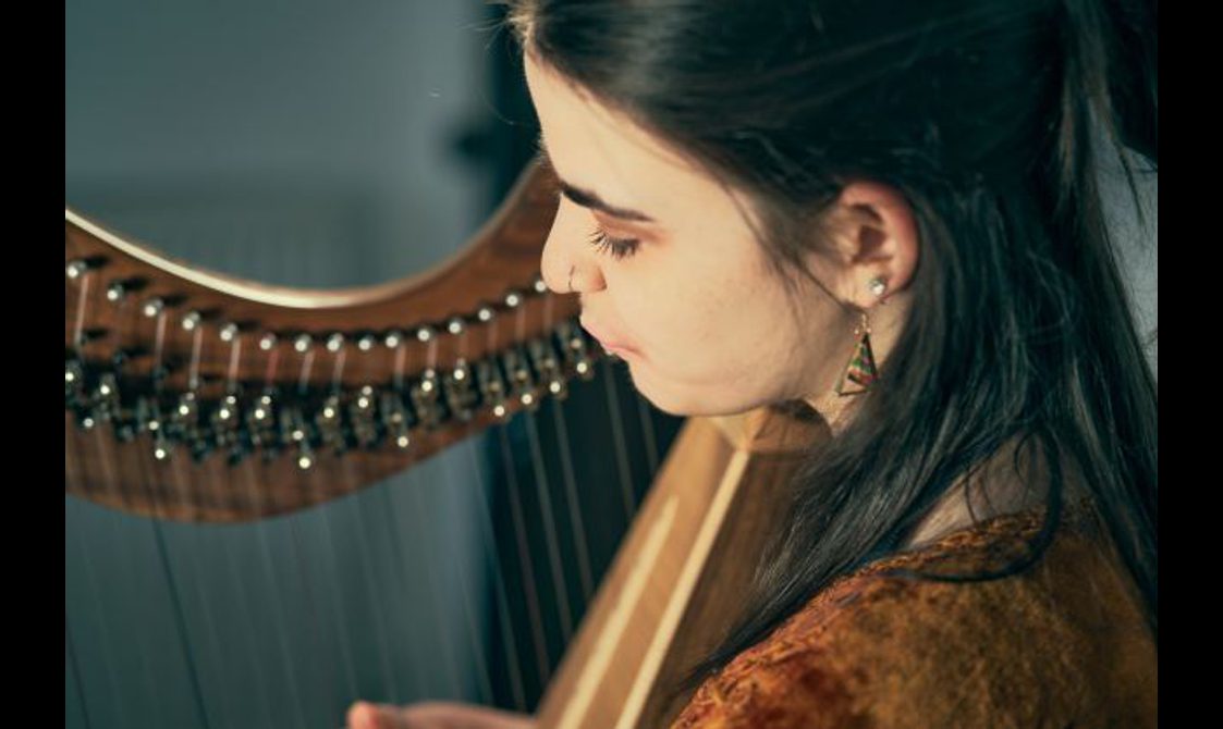 Close up of a young woman playing a wooden harp-like instrument.