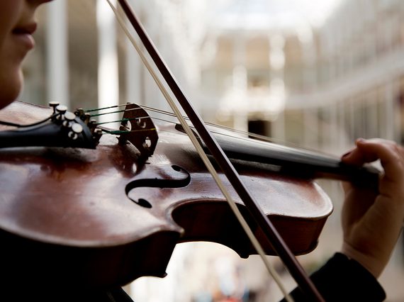 A close up of a musician playing a violin with the Grand Gallery in the background.