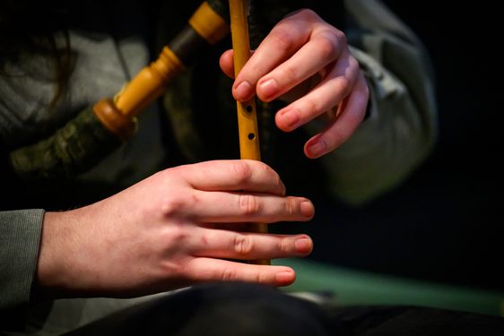 Close up of two hands playing the wooden flute of a bagpipe. The bagpipe held under the arm is in soft focus.