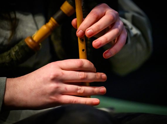Close up of two hands playing the wooden flute of a bagpipe. The bagpipe held under the arm is in soft focus.