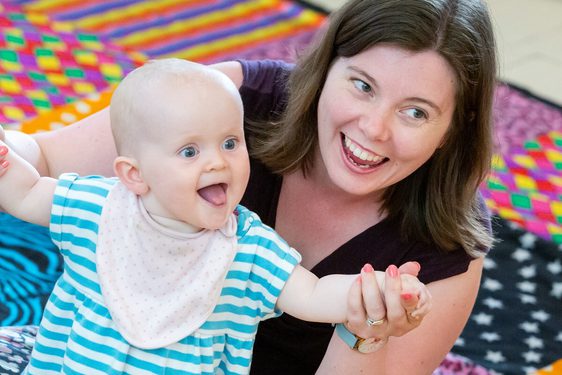 Woman and baby in arms sitting on the floor on a checked carpet.
