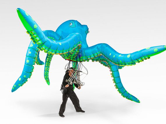 A person controlling a large inflatable illuminated octopus puppet.