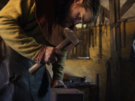 A blacksmith wearing a beige apron hits metal with a hammer.