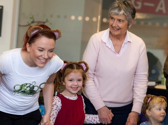 An intergenerational family are wearing monkey ears and holding hands. They look very happy.