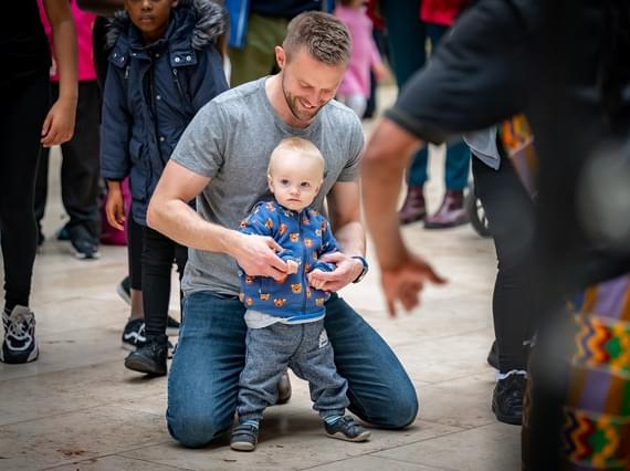 A youg child and his parent or carer are surrounded by a crowd of people and enjoying an event in the grand gallery at the National Museum of Scotland.