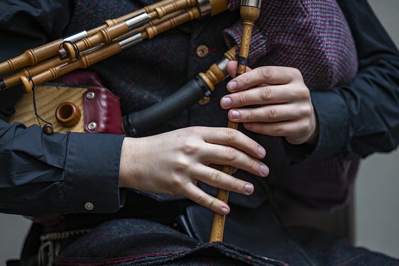 A close up image of a person in dark clothes against a grey background playing a set of wooden small pipes