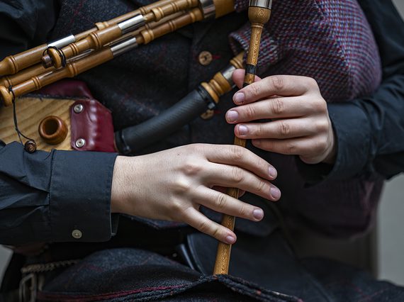 A close up image of a person in dark clothes against a grey background playing a set of wooden small pipes
