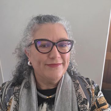 A headshot of Lisa Williams. She has long curly hair and is wearing back cat-eye glasses.