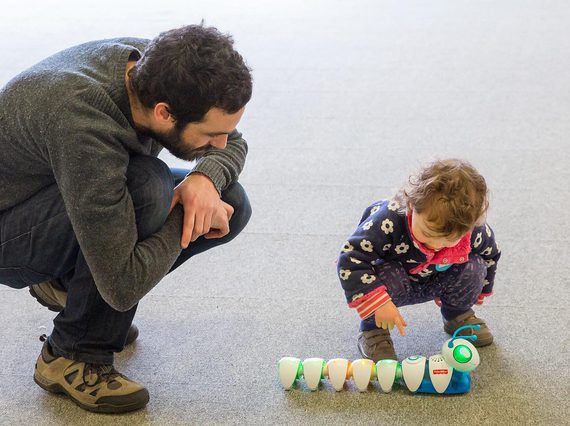 A parent and child crouching down, playing with a robotic caterpillar toy.