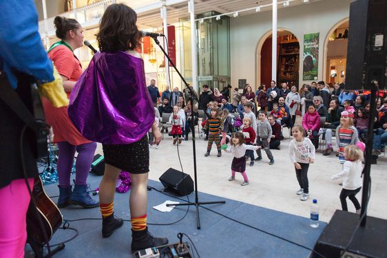 Performers dressed as superheroes singing on a stage to an audience of families and young children.