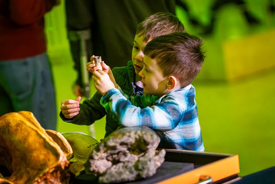 Two children examine museum objects on a trolley. One is holding a small bone while the other looks intently.