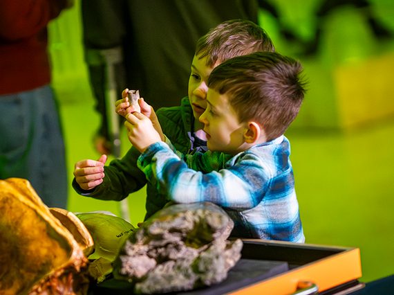 Two children examine museum objects on a trolley. One is holding a small bone while the other looks intently.