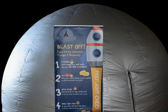 A large inflatable silver dome against a black background. In front of the dome, there is a pop-up banner with instructions of the space experience inside the dome with an illustration of a rocket.