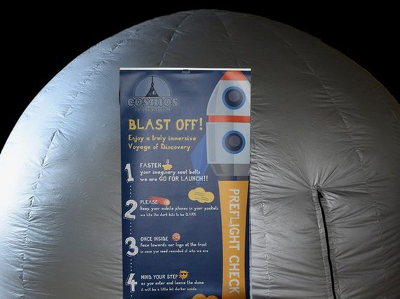 A large inflatable silver dome against a black background. In front of the dome, there is a pop-up banner with instructions of the space experience inside the dome with an illustration of a rocket.
