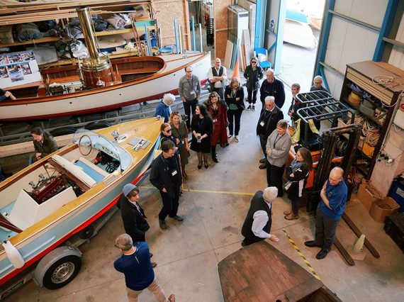 A group of people standing in a museum store. The store contains different boats from maritime history.