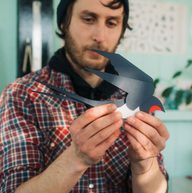 A man holding a papercut swallow in his hands, in an artist's studio.