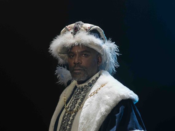 Film still of a 16th century Black African diplomat dressed in elaborate European-style clothing with a thick, white fur trimmed collar and hat. He is holding a scroll.