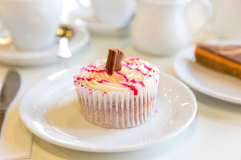 Close up of a cupcake with white icing, raspberry sauce, and a chocolate flake.