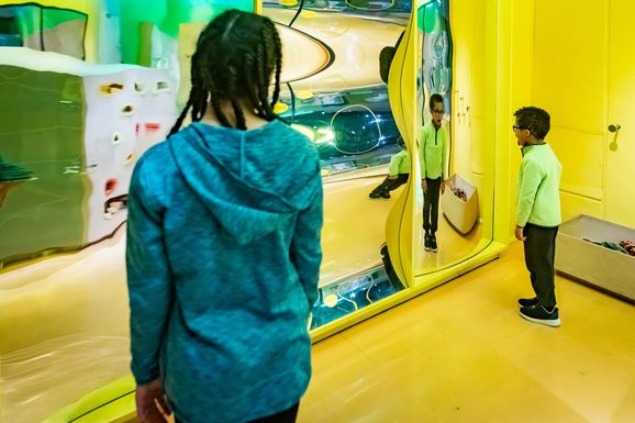 Two visitors staring at their reflections in an interactive mirror display.