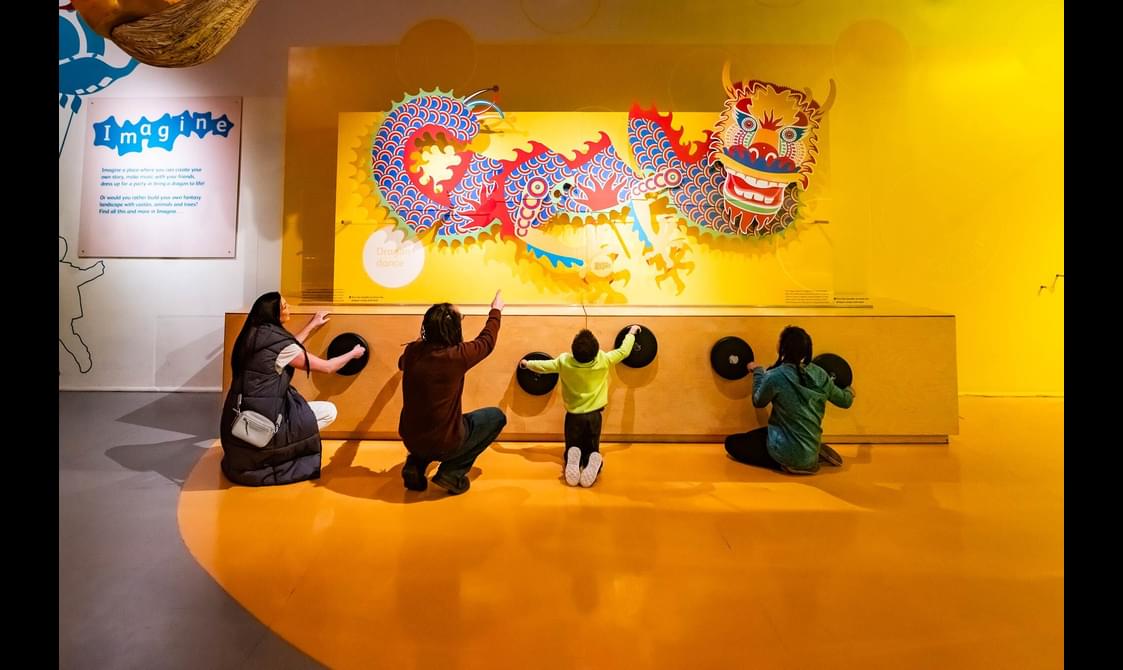 A family of four turning wheels to move a colourful dragon model on a wall above.